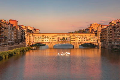 View of ponte vecchio bridge glittering in sunset sun beams, river arno at golden hour.