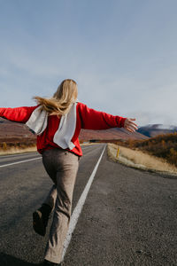 Woman in a red jumper and a scarf running on the road in iceland with arms spread