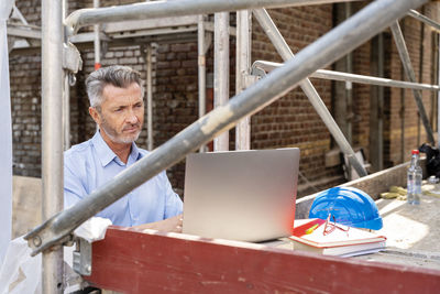 Professional working on laptop while sitting at construction site