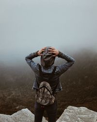 Rear view of woman standing on rock against sky