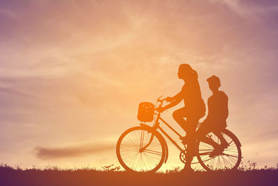 Silhouette people with bicycle against sky during sunset