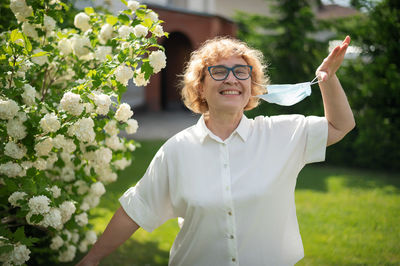 Smiling young woman standing by white flowering plants