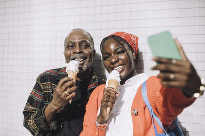 Smiling man taking selfie with father eating ice cream during sunny day