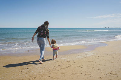 Rear view of woman walking at beach against sky