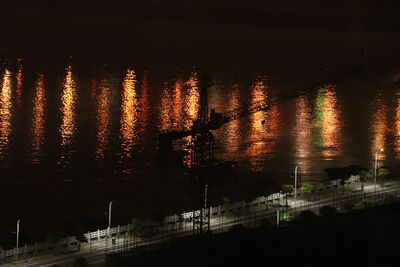 Silhouette city by lake against sky at night