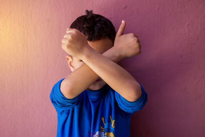 Boy with arms crossed standing against wall