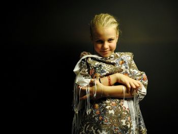 Portrait of smiling girl standing against black background