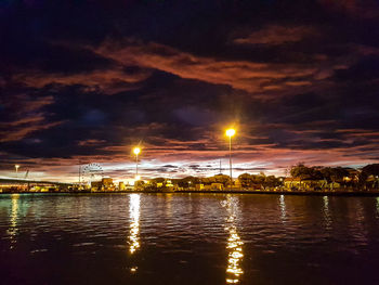 Illuminated city by river against sky at night