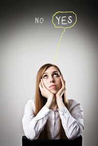 Portrait of young woman looking up against wall