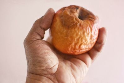 Close-up of hand holding apple against white background