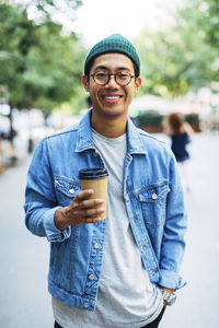 Portrait of happy man with hand in pocket holding disposable cup at sidewalk