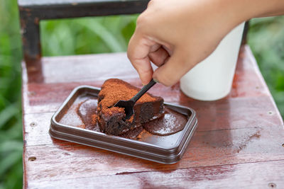 Close-up of hand holding chocolate cake on table