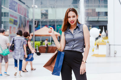 Portrait of smiling young woman with shopping bags standing outside in mall