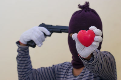 Close-up of man holding heart shape and gun against wall