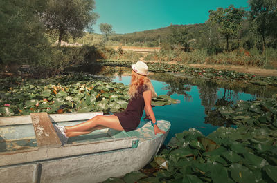 Carefree young woman floating relaxed on a boat at a pond with blooming waterlily, lotus flowers.