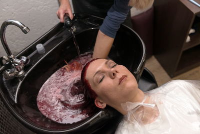 Female hairdresser washes of woman head on a sink after dyeing hair in the salon on the working day.