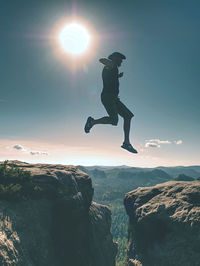 Jumping against sun. jumps over cliff. active mn jump between mountain tops. man fly over deep gulch