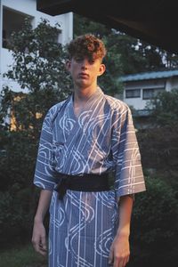 Portrait of young man wearing traditional clothing standing against house