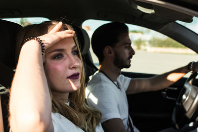 Side view of positive relaxed young woman enjoying view from passenger seat during road trip with boyfriend in sunny summer day