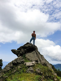 Low angle view of man standing on rock against sky