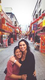 Portrait of smiling young woman with arms raised in city