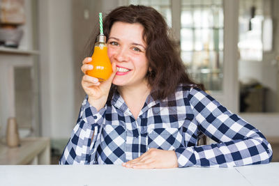 Portrait of smiling woman holding juice sitting at cafe