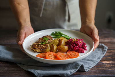 Hands holding plate with cooked meat and veggies