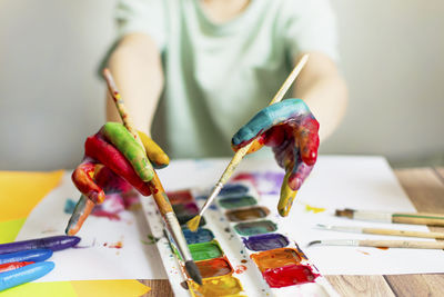 Cropped hand of boy holding paintbrush over palette while painting at classroom