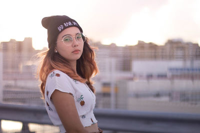 Portrait of young woman wearing sunglasses standing against sky during sunset