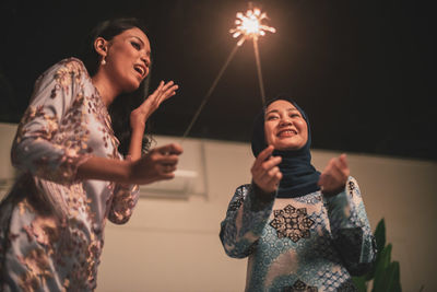 Happy woman standing by illuminated lighting equipment