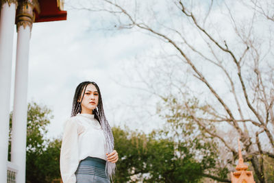 Portrait of young woman standing by tree against plants