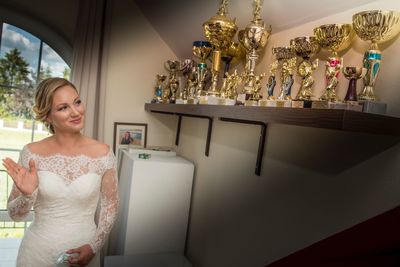 Smiling bride waving hand while looking at trophies on shelf