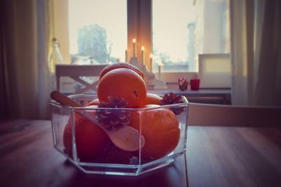 Close-up of orange fruits and pine cones in glass container against window