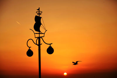 Silhouette bird flying against orange sky