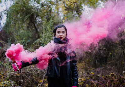 Portrait of young woman holding distress flare while standing in forest