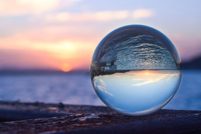 Close-up of crystal ball against sea during sunset