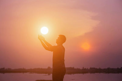 Side view of silhouette man standing against bright sun during sunset