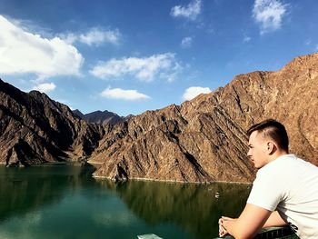 Boy standing on rock by lake against sky