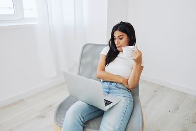 Young woman using laptop while sitting on sofa at home