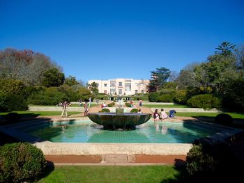 People near fountain in garden against clear blue sky