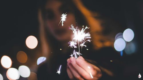 Low angle view of woman burning sparkler while standing on street at night