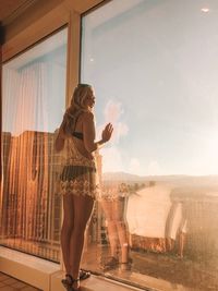 Side view of woman standing by glass window in room