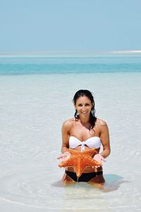 Portrait of smiling young woman holding starfish at beach