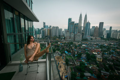 Woman looking at city while sitting on chair in balcony