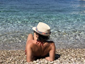 Rear view of woman relaxing at beach against sky