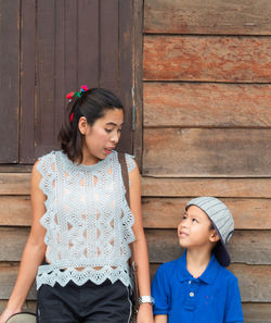 Mother and son standing by wooden house