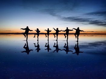 Silhouette people dancing at beach against sky during sunset