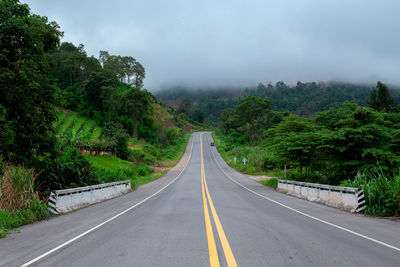 Empty road along trees and against sky