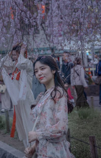 Young woman standing by cherry blossom tree