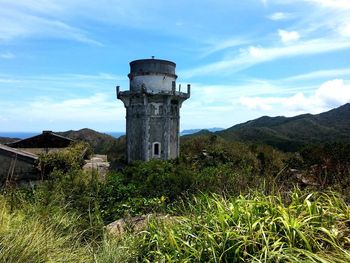 Lighthouse in front of green mountains against blue sky